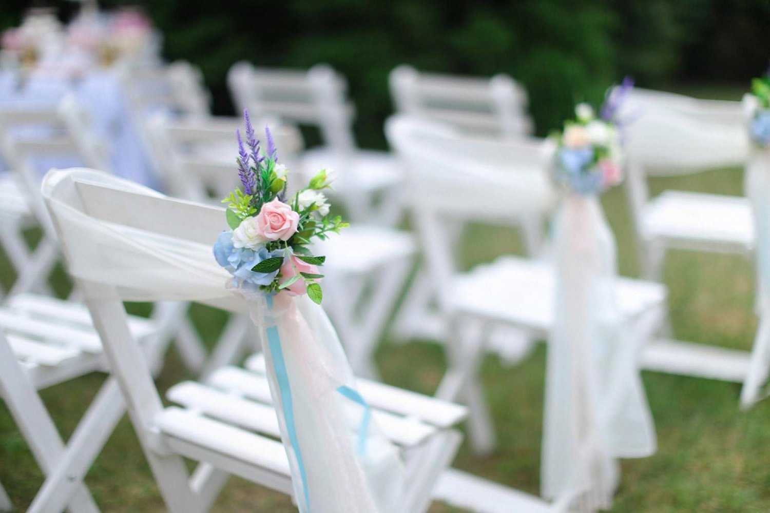 White garden ceremony chairs decorated with pastel floral arrangements and ribbons at a UAE outdoor wedding
